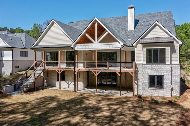 rear view of house featuring a chimney, roof with shingles, stairway, brick siding, and a patio