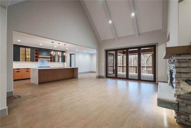 unfurnished living room with visible vents, a fireplace, high vaulted ceiling, baseboards, and light wood finished floors