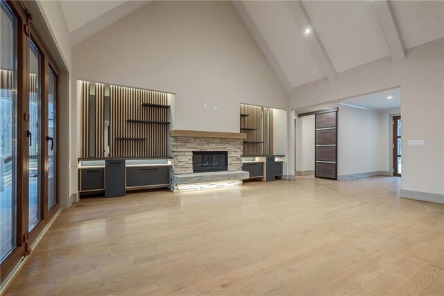 unfurnished living room featuring a fireplace, high vaulted ceiling, baseboards, beamed ceiling, and light wood-style flooring