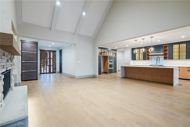unfurnished living room featuring baseboards, high vaulted ceiling, a fireplace with raised hearth, a sink, and light wood-style flooring