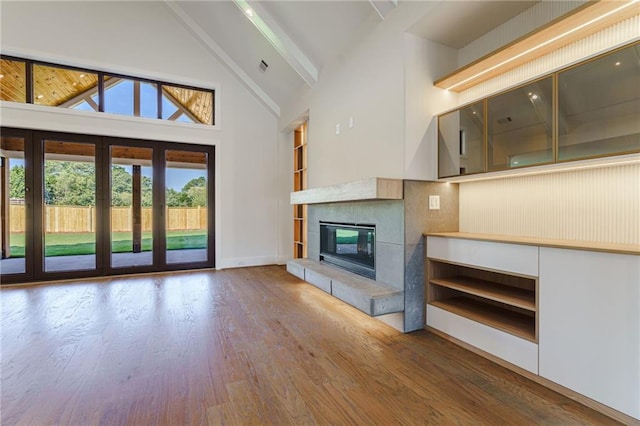 unfurnished living room featuring high vaulted ceiling, a tiled fireplace, baseboards, wood finished floors, and beamed ceiling