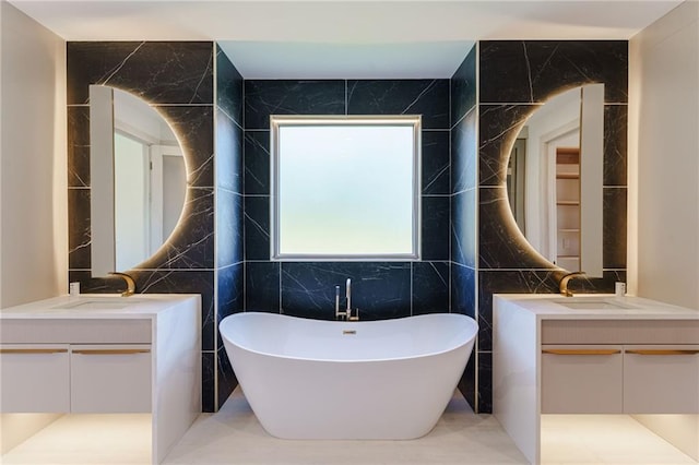 full bath featuring a soaking tub, tile walls, two vanities, and a sink