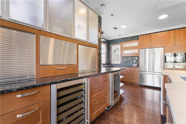 kitchen with stainless steel built in fridge, ornamental molding, dark stone countertops, and beverage cooler