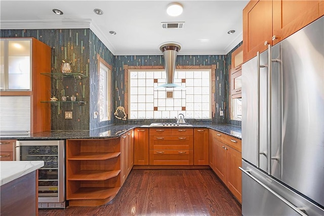 kitchen with dark wood-type flooring, dark stone counters, wine cooler, ornamental molding, and appliances with stainless steel finishes