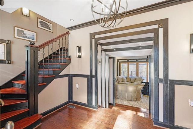 entrance foyer with an inviting chandelier, wood-type flooring, and ornamental molding