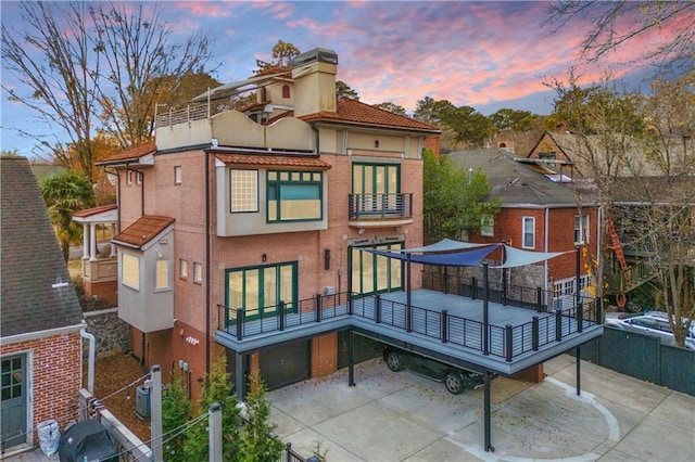 back house at dusk with a garage and a balcony