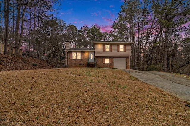 split level home featuring concrete driveway, a chimney, an attached garage, a yard, and brick siding