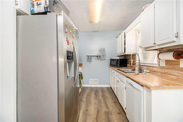 kitchen with black microwave, white dishwasher, a sink, visible vents, and stainless steel refrigerator with ice dispenser