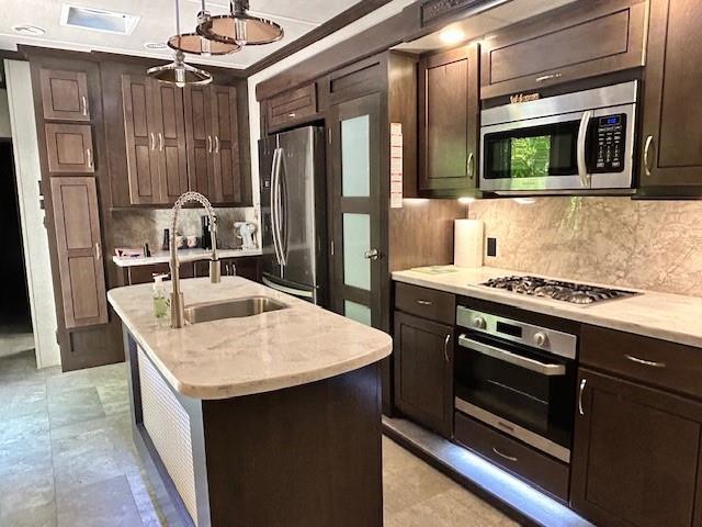 32 7th St, Ellijay, GA 30540 - kitchen with appliances with stainless steel finishes, a sink, tasteful backsplash, a center island with sink, and dark brown cabinetry
