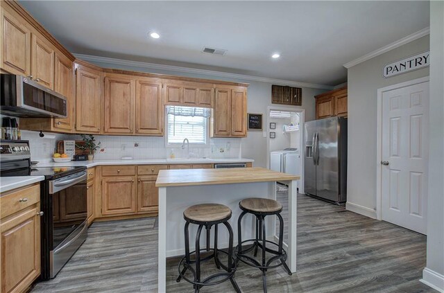 kitchen featuring butcher block counters, stainless steel appliances, wood-type flooring, crown molding, and washing machine and clothes dryer