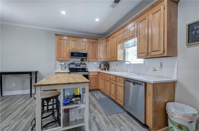 kitchen with appliances with stainless steel finishes, crown molding, decorative backsplash, and light hardwood / wood-style floors