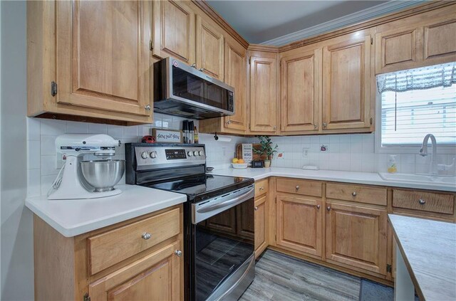 kitchen with stainless steel appliances, backsplash, crown molding, sink, and light hardwood / wood-style floors