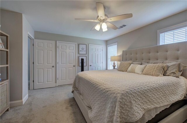 bedroom with two closets, multiple windows, light colored carpet, and ceiling fan