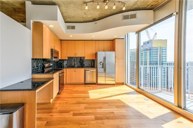 kitchen with a healthy amount of sunlight, sink, decorative backsplash, appliances with stainless steel finishes, and light hardwood / wood-style floors