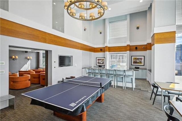 game room featuring carpet floors, a towering ceiling, and a notable chandelier