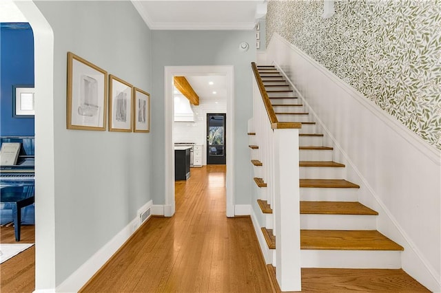 staircase featuring beam ceiling, wood-type flooring, and ornamental molding