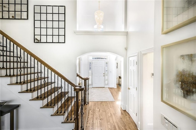 entryway featuring arched walkways, visible vents, a towering ceiling, and wood finished floors