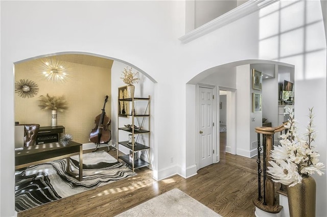 interior space with a high ceiling, baseboards, arched walkways, and wood finished floors