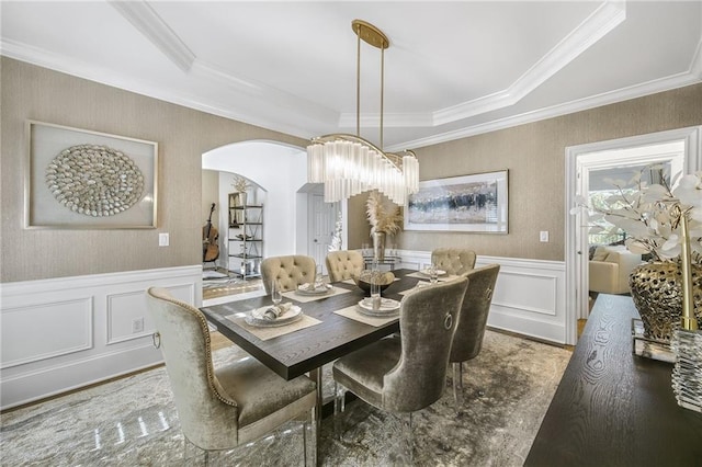 dining area featuring ornamental molding, arched walkways, a wainscoted wall, and wood finished floors