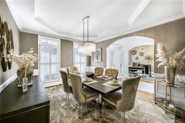 dining space featuring ornamental molding, arched walkways, wainscoting, and wood finished floors