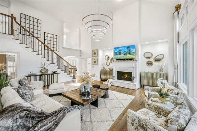 living room featuring a warm lit fireplace, radiator, stairway, wood finished floors, and crown molding