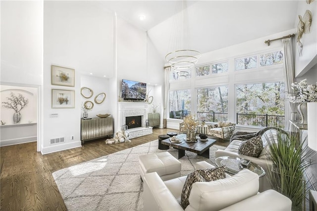 living area featuring a warm lit fireplace, visible vents, a high ceiling, and wood finished floors