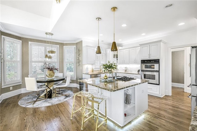 kitchen with a wealth of natural light, appliances with stainless steel finishes, wood finished floors, and light stone counters