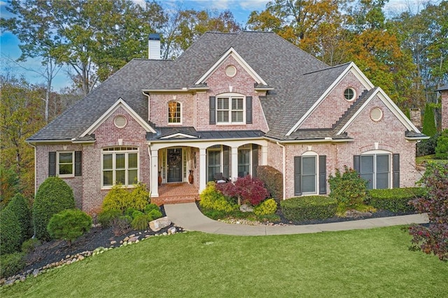 traditional-style house featuring covered porch, a front lawn, a chimney, and brick siding