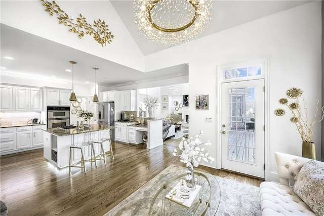 living room with dark wood-style floors, a notable chandelier, high vaulted ceiling, and crown molding