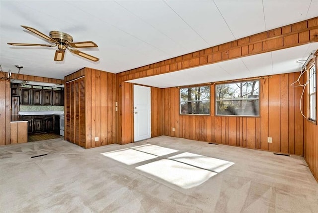 unfurnished living room featuring light carpet, wooden walls, and ceiling fan