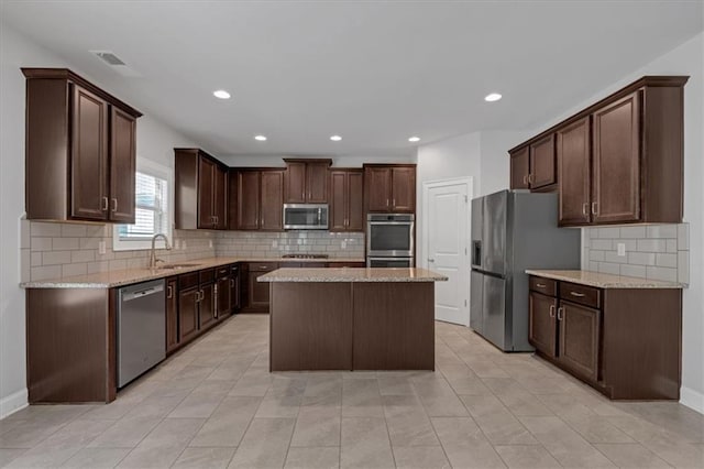 kitchen featuring sink, appliances with stainless steel finishes, dark brown cabinets, light stone counters, and a kitchen island