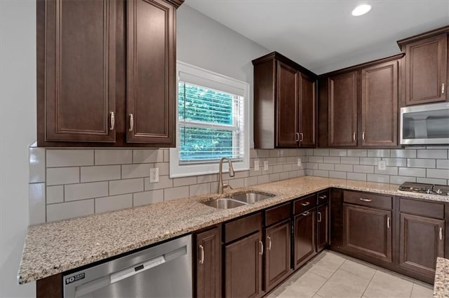 kitchen with sink, tasteful backsplash, light tile patterned floors, appliances with stainless steel finishes, and light stone countertops