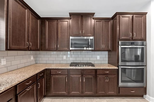 kitchen with stainless steel appliances, light stone countertops, dark brown cabinets, and backsplash