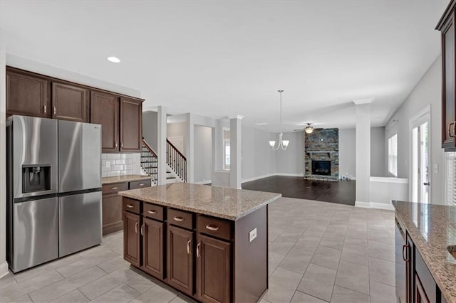 kitchen featuring stainless steel refrigerator with ice dispenser, light stone counters, decorative light fixtures, a center island, and dark brown cabinets