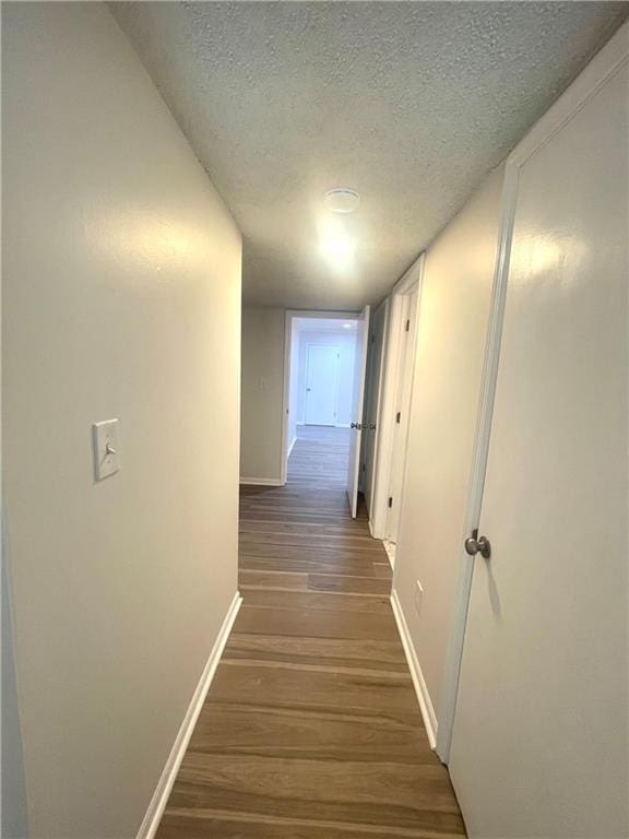 hallway featuring a textured ceiling, baseboards, and wood finished floors