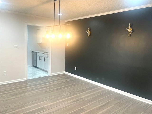 unfurnished dining area featuring light wood finished floors, a textured ceiling, crown molding, and baseboards