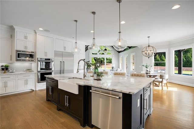 kitchen with sink, white cabinetry, hanging light fixtures, a kitchen island with sink, and built in appliances