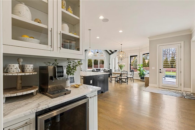 bar with wine cooler, decorative light fixtures, light stone countertops, and crown molding