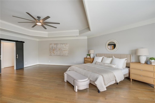 bedroom with crown molding, a tray ceiling, a barn door, and hardwood / wood-style flooring