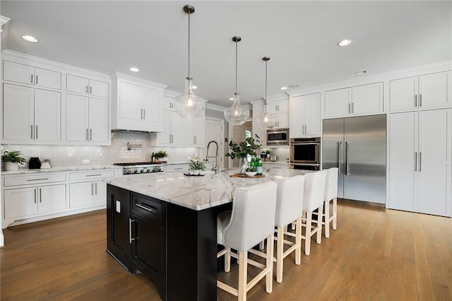 kitchen featuring white cabinetry, built in appliances, hanging light fixtures, a center island with sink, and hardwood / wood-style flooring