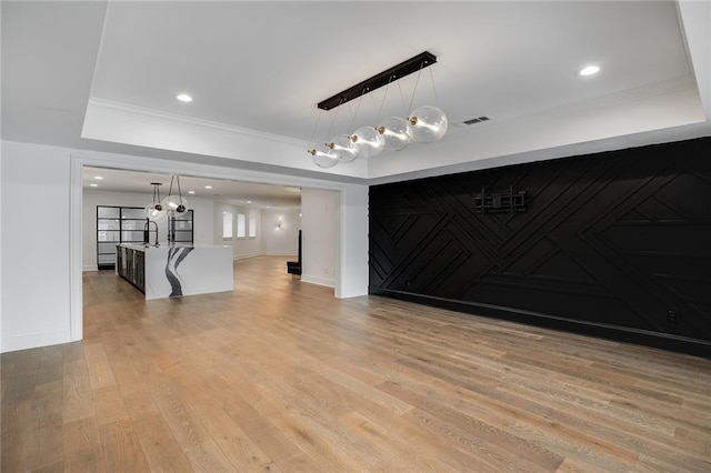 interior space featuring crown molding, a raised ceiling, and light hardwood / wood-style flooring