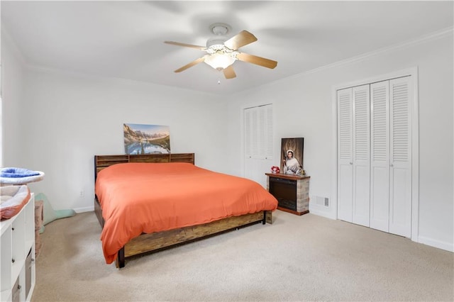 carpeted bedroom with two closets, ornamental molding, and ceiling fan