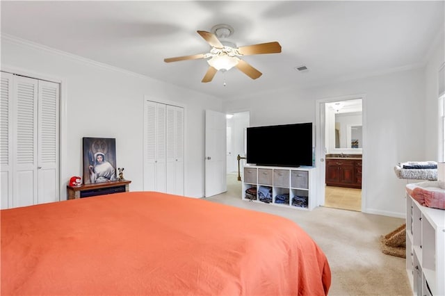 carpeted bedroom featuring multiple closets, ensuite bath, and ceiling fan