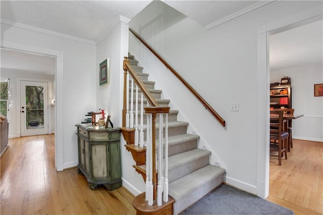 staircase with crown molding, wood-type flooring, and a textured ceiling