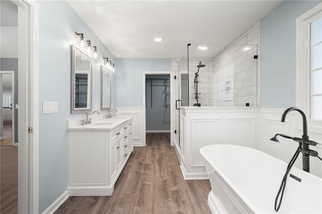 bathroom with wood finished floors, a soaking tub, double vanity, a stall shower, and a sink