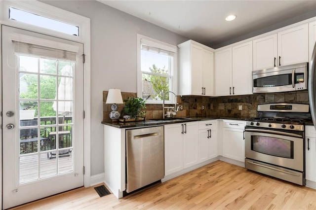 kitchen with decorative backsplash, visible vents, appliances with stainless steel finishes, a sink, and light wood-style flooring