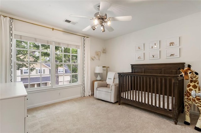 bedroom with visible vents, baseboards, light colored carpet, a nursery area, and a ceiling fan