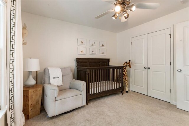bedroom with a ceiling fan, a nursery area, light carpet, and a closet