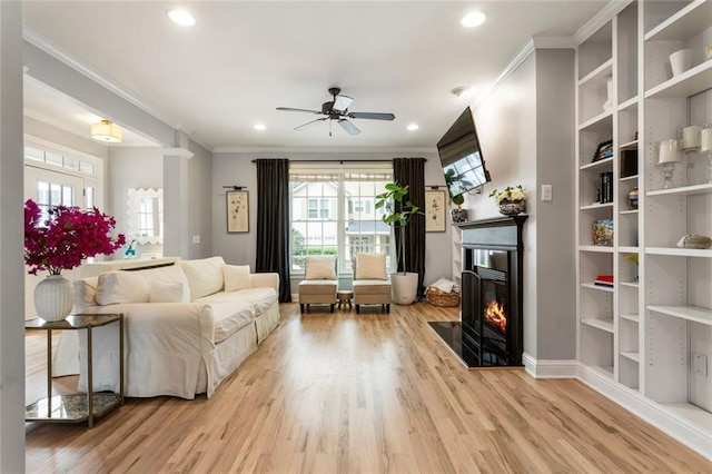 living area with ornamental molding, a fireplace with flush hearth, a ceiling fan, and a wealth of natural light