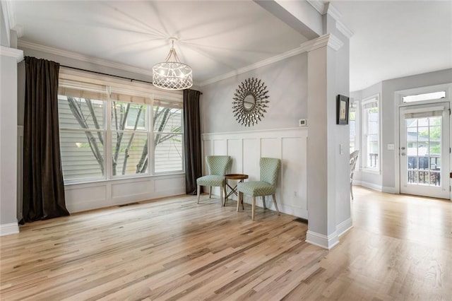 living area with a decorative wall, a chandelier, wood finished floors, visible vents, and ornamental molding